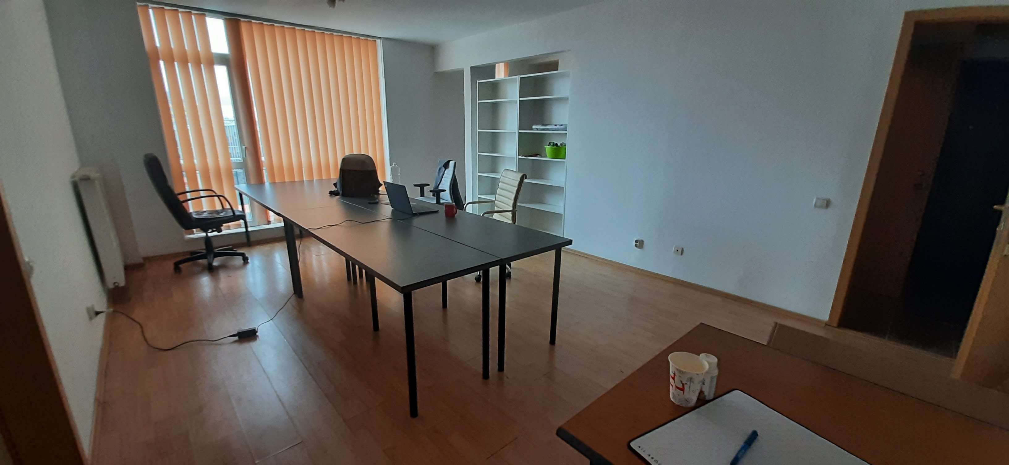 The main room - sparse, just 2-3 desks, orange window blinds